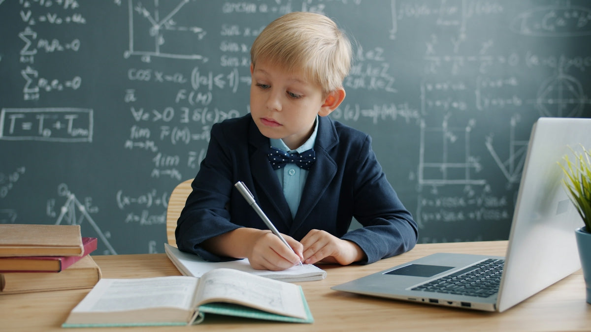Young boy in a suit writing at a desk.