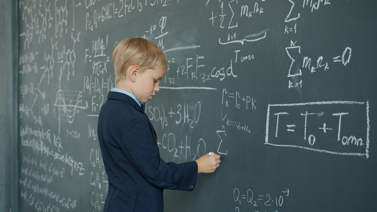 Young boy in suit writing math equations on blackboard