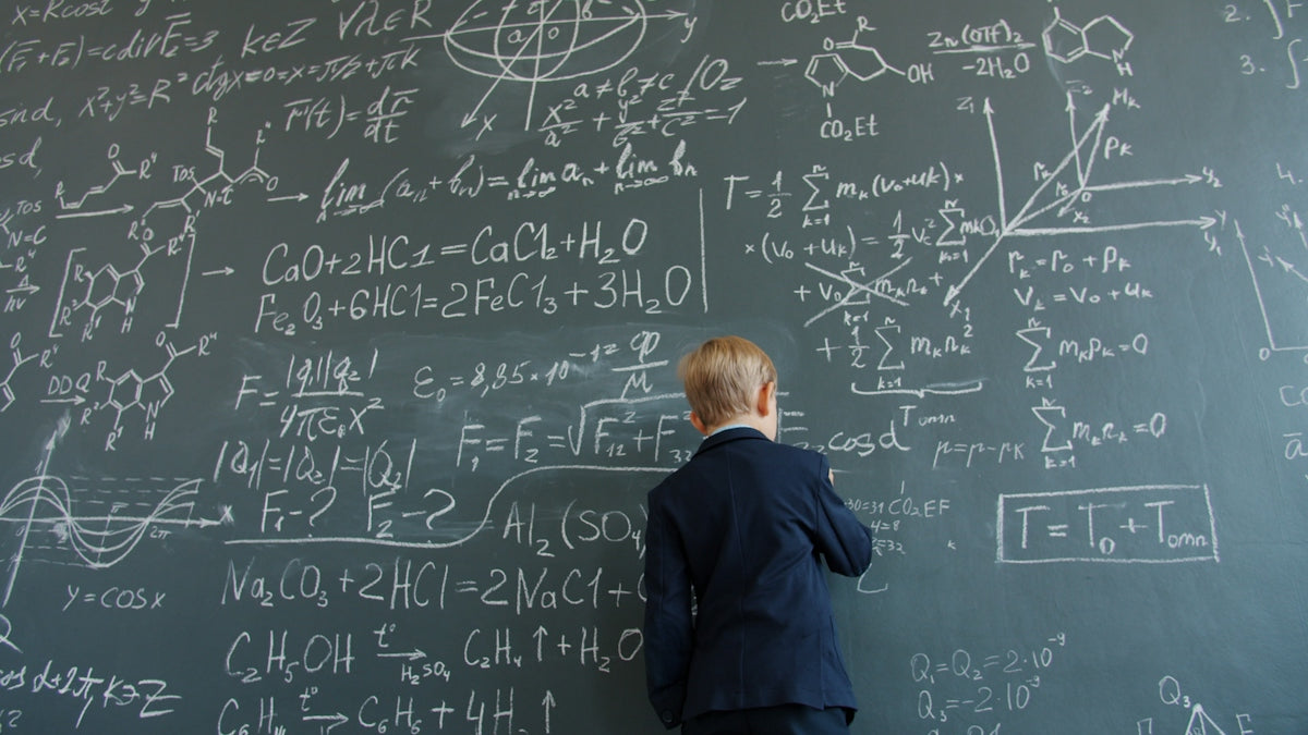 Young boy in suit writing on chalkboard with formulas